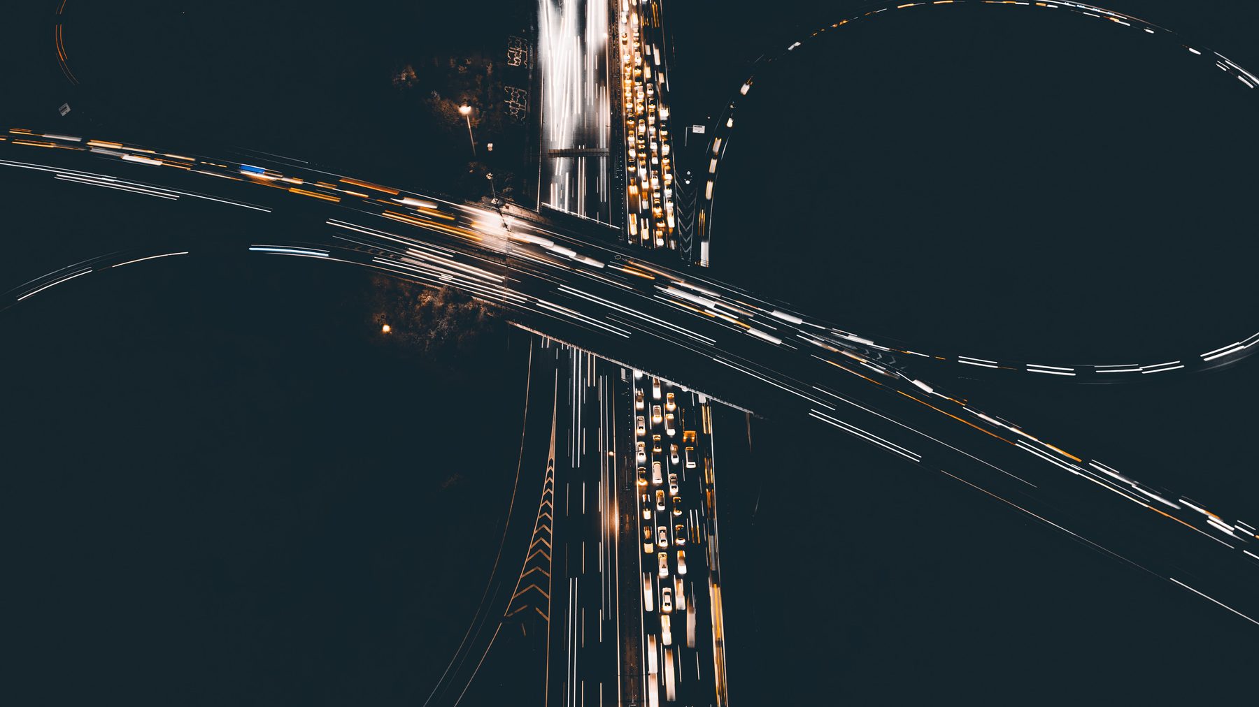 A motorway interchange seen from the air at night, traffic drawn out into long light trails.